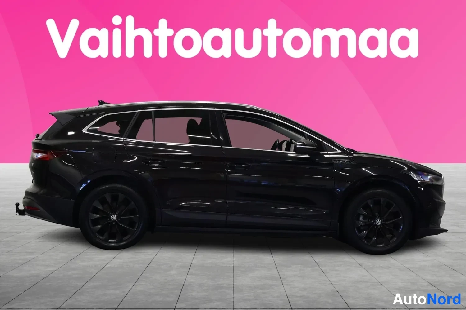 Sivulta: Mustan farmariauton sivuprofiili, keskittyliike Vahtoautomanan vaaleanpunaisella taustalla