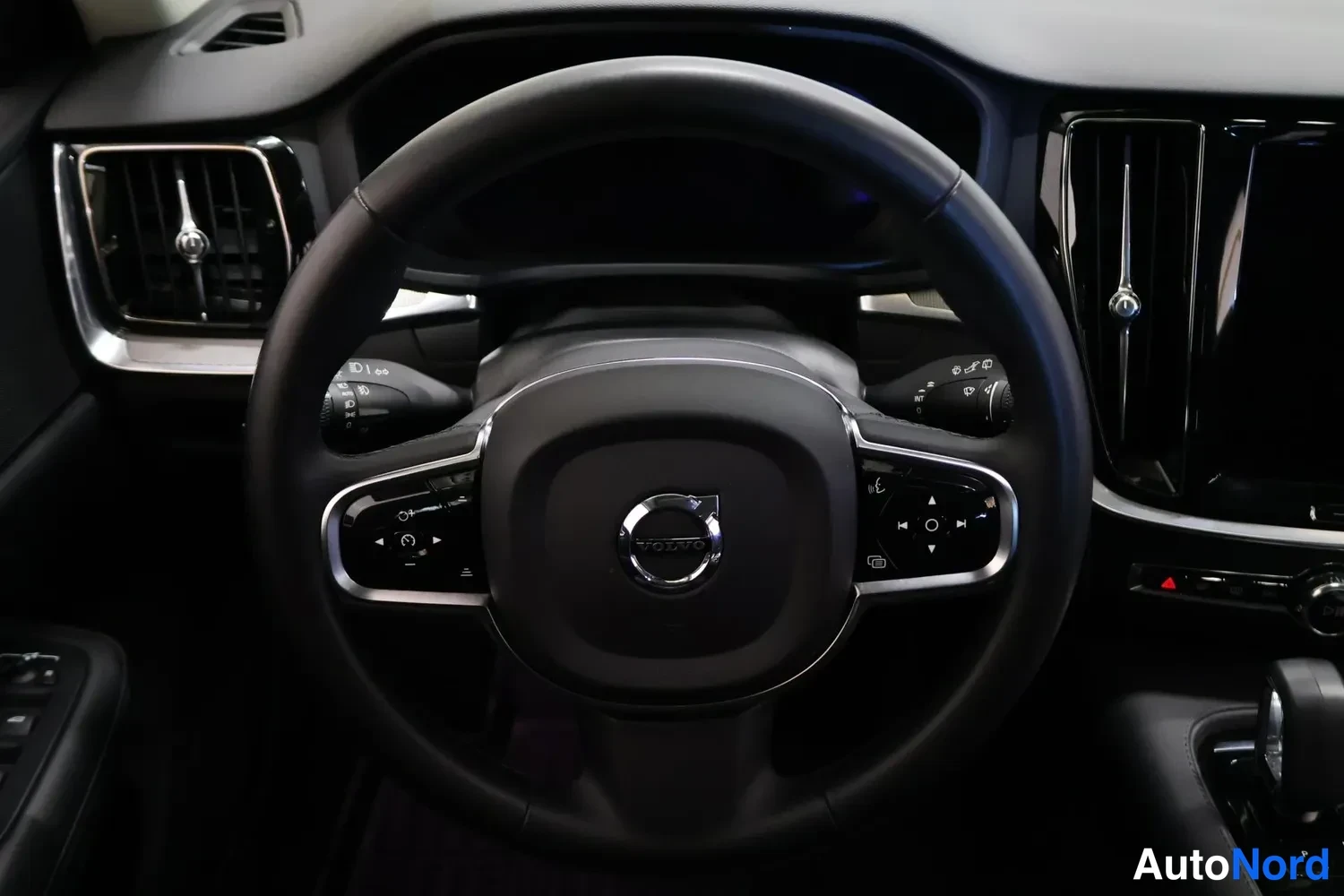 Muu: Volvo-ohjauspyörä ja kojelaudan vasen osa: ilmastointilaitteet ja keskynäytön reuna näkyvät.