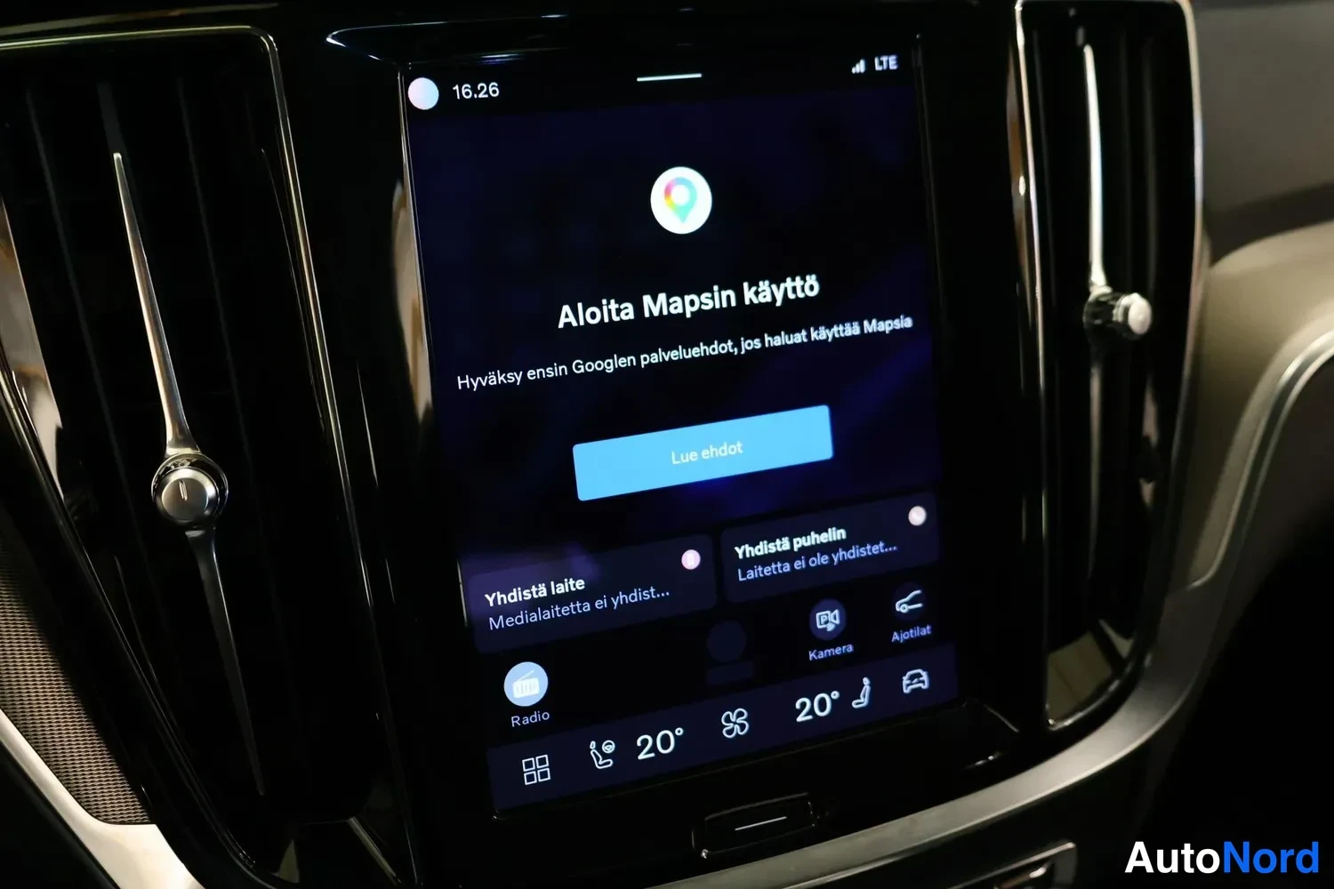 Yksityiskohta: Close-up of vertical central infotainment screen in a car's interior dashboard. Screen shows Google Maps setup 'Aloita Mapsin käyttö' (Start Map use) at 16:26 w