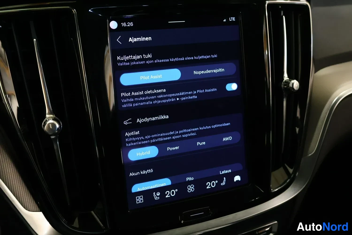Yksityiskohta: Center infotainment touchscreen in driving settings menu titled 'Ajaminen' (Driving). Driver assistance section shows Pilot Assist toggle active and text about