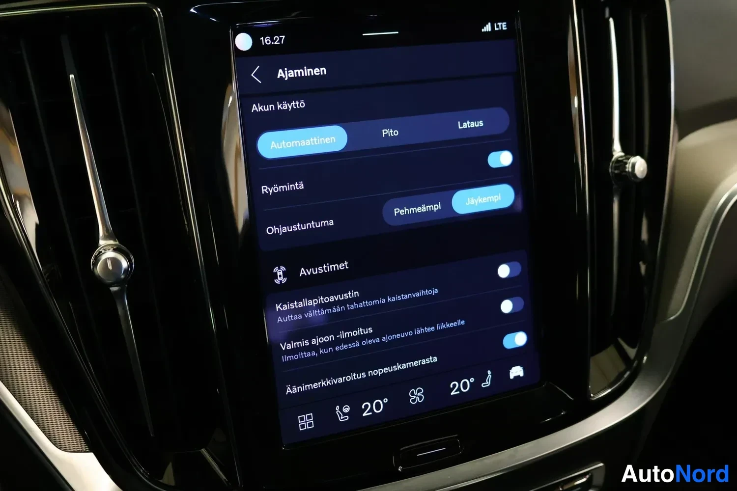Yksityiskohta: Infotainment screen displaying vehicle settings under battery usage heading 'Akun käyttö' set to Automatic. Chassis selection menu below offers Pehmeämpi (softe