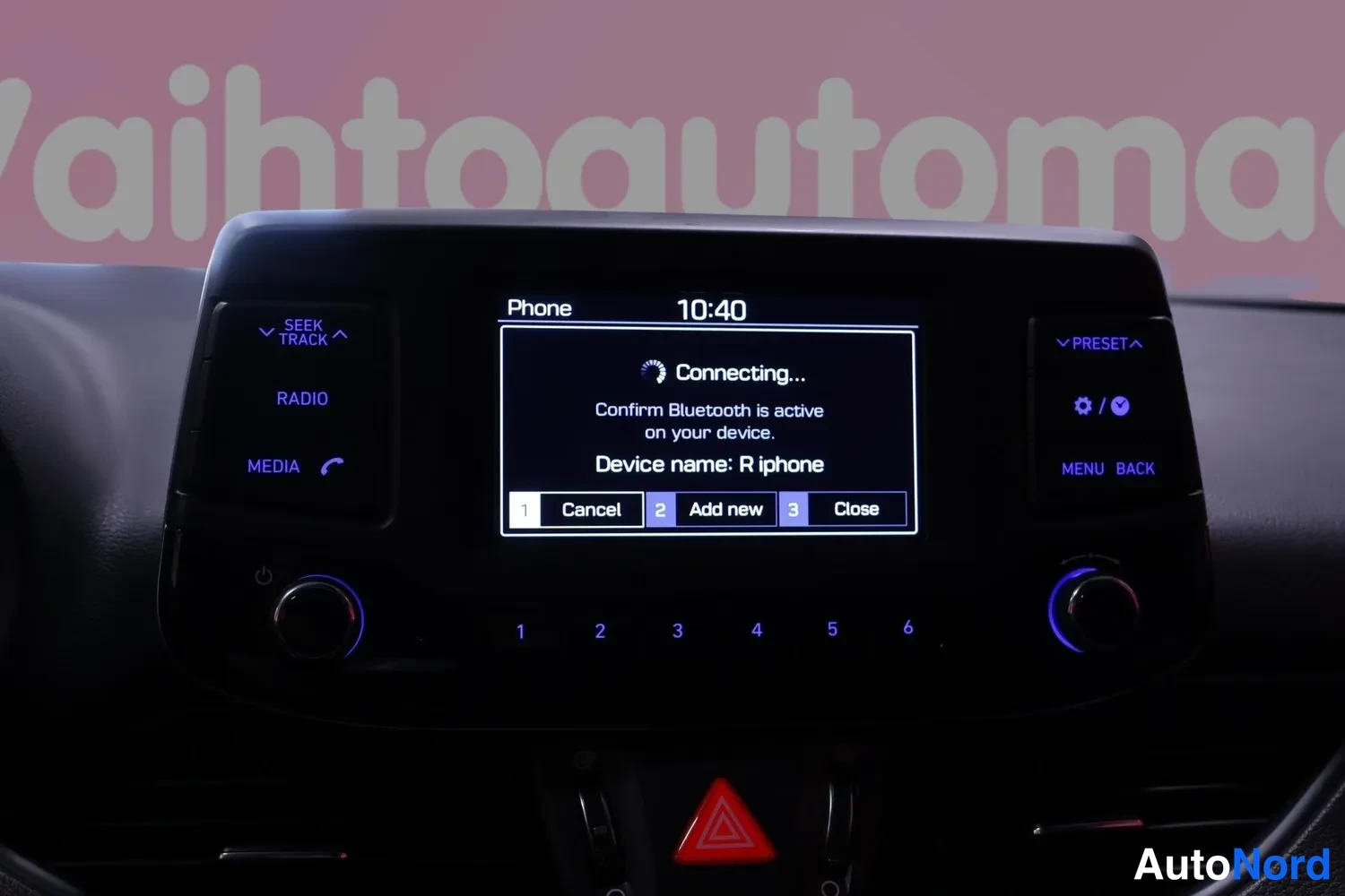 Yksityiskohta: Auton kojelaudan infotainment-näyttö näyttää puhelimen Bluetooth-kytkentäruudun tekstillä Connecting... ja laitteen nimellä R iphone.