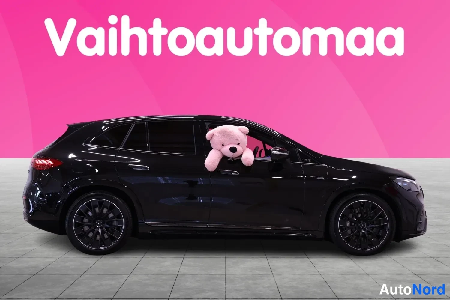 Etuviisto, nokka oikealle: Musta Mercedes-Benz EQE SUV sivulta etukolmasta, pinkki tausta ja nalle ikkunassa.