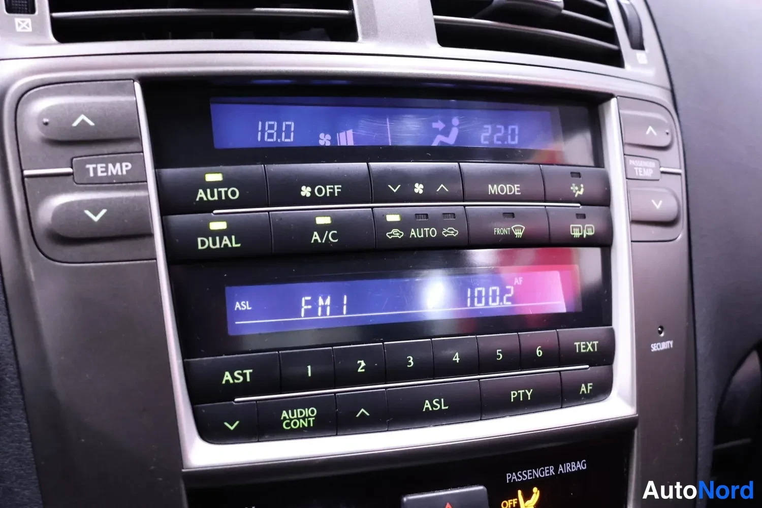 Muu: Keskikonsolin ilmastointipaneeli, näytöllä lämpötilat 18.0 ja 22.0, painikkeet AUTO, DUAL, A/C ja MODE, sekä radiopaneeli, näytöllä FM1 100.2.