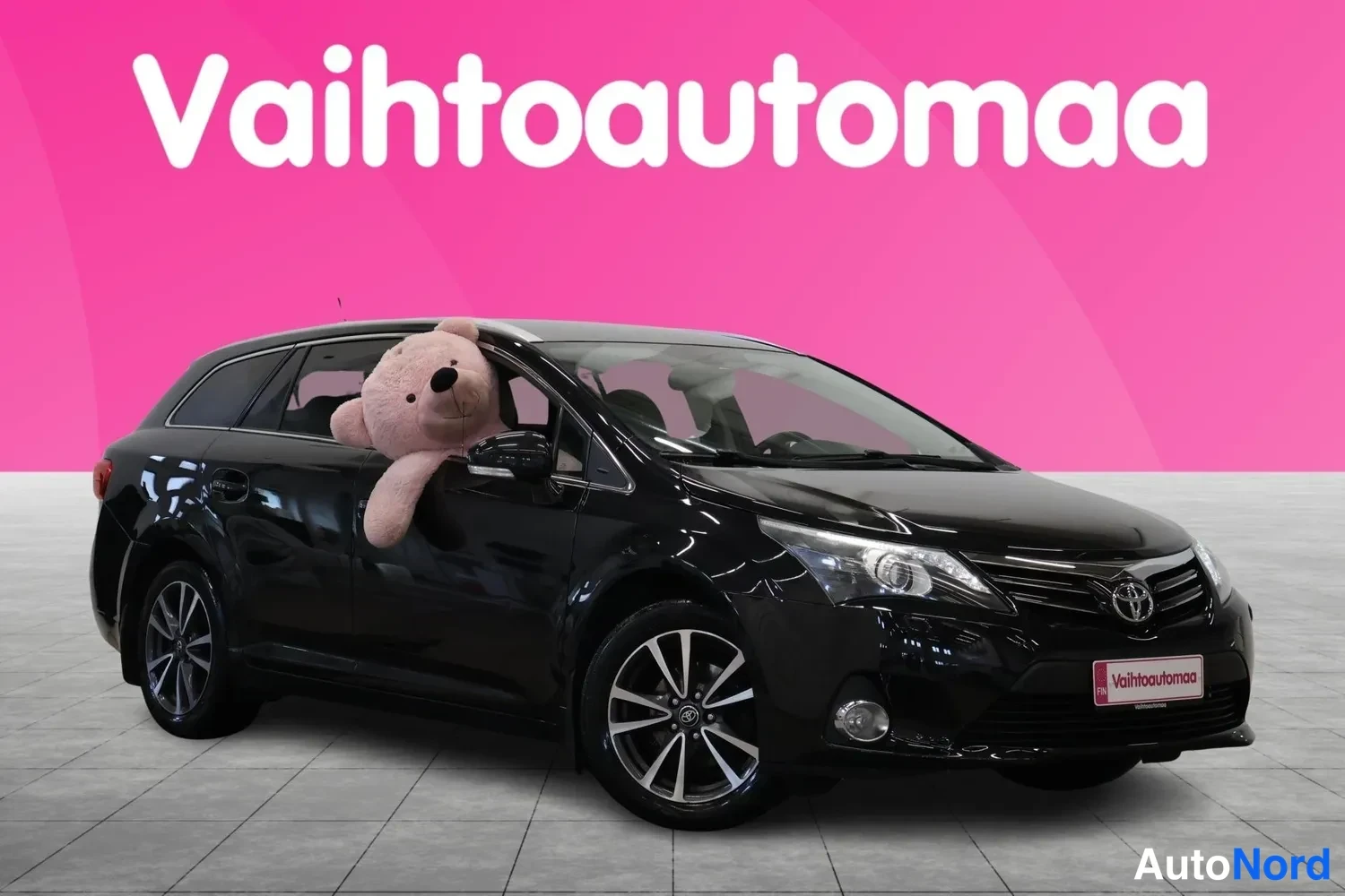 Etuviisto, nokka oikealle: Musta Toyota Avensis -farmari kuvattu kolmesta neljäsosasta keula oikealla, suurpeili ja kevytmetallivanteet näkyvissä.