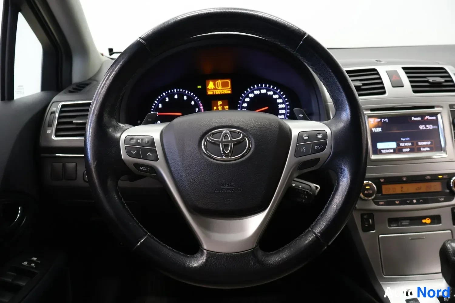 Yksityiskohta: Ohjauspyörän tarkempi kuva: Toyota-merkki, SRS AIRBAG-teksti, mittaristo ja radiopaneeli näytöllä 95.50.