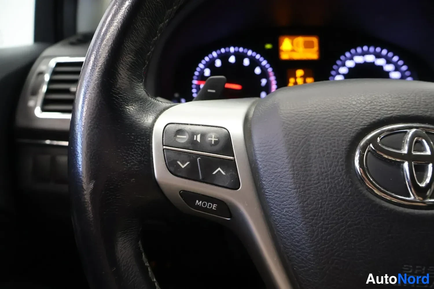 Muu: Toyota-merkillä varustetun ohjauspyörän vasen puhallus, jossa äänenvoimakkuus- ja MODE-painikkeet.