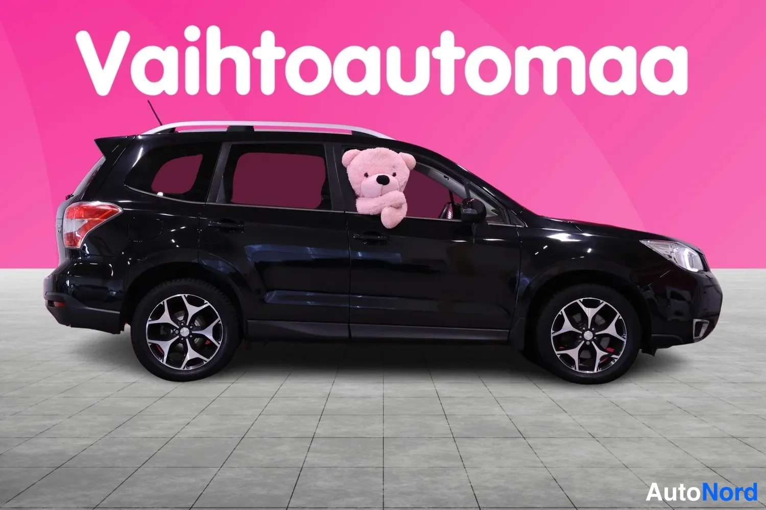 Sivulta: Musta Subaru Forester sivulta kuvattuna, keula oikealla; kattokaiteet ja kaksiväriset kevytmetallivanteet näkyvät.