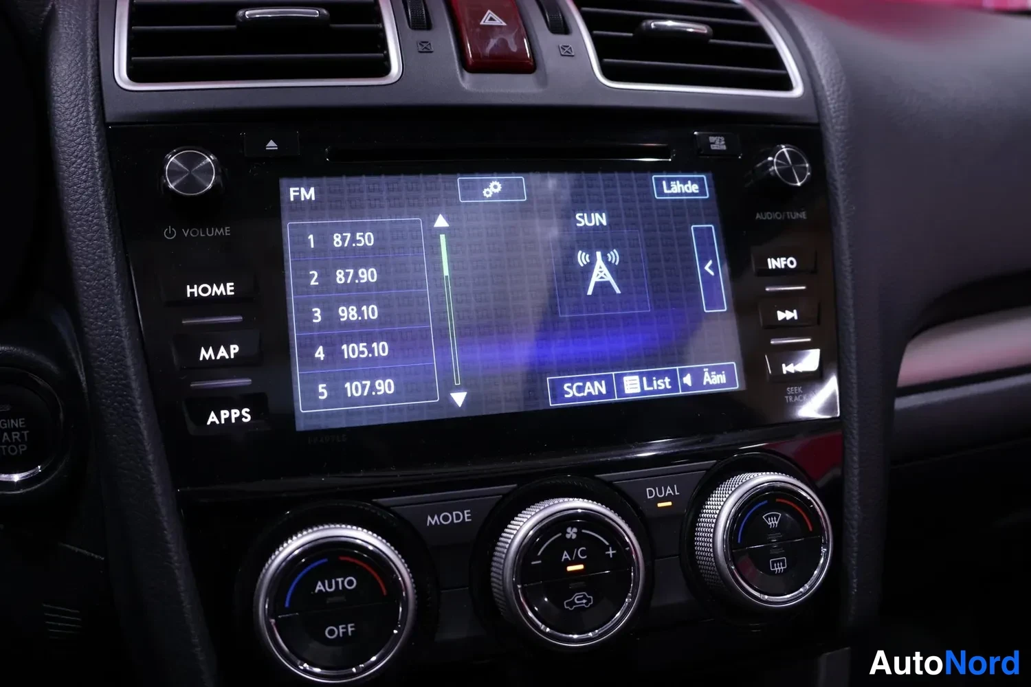 Yksityiskohta: Keskikonsolin näyttö radiotoiminnoissa FM-taajuuksilla 87.50–107.90, ylhäällä varoitusvalo, alla AUTO ja A/C-säätimet.