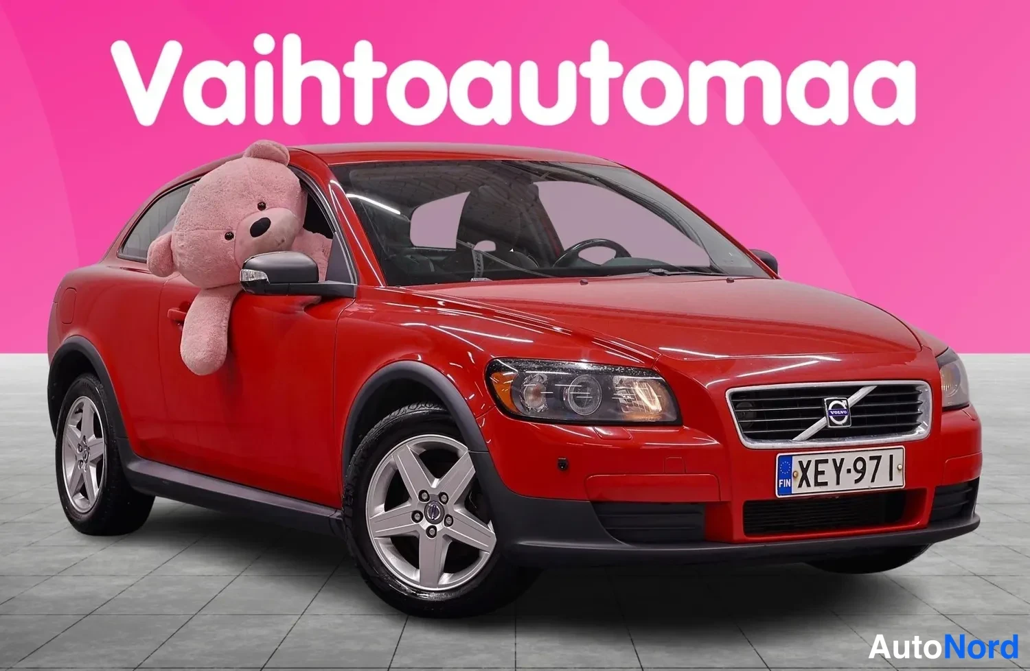 Etuviisto, nokka oikealle: Punainen kolmiovinen henkilöauto kolmannesovelta etusta oikealta, rekisterikilpi.
