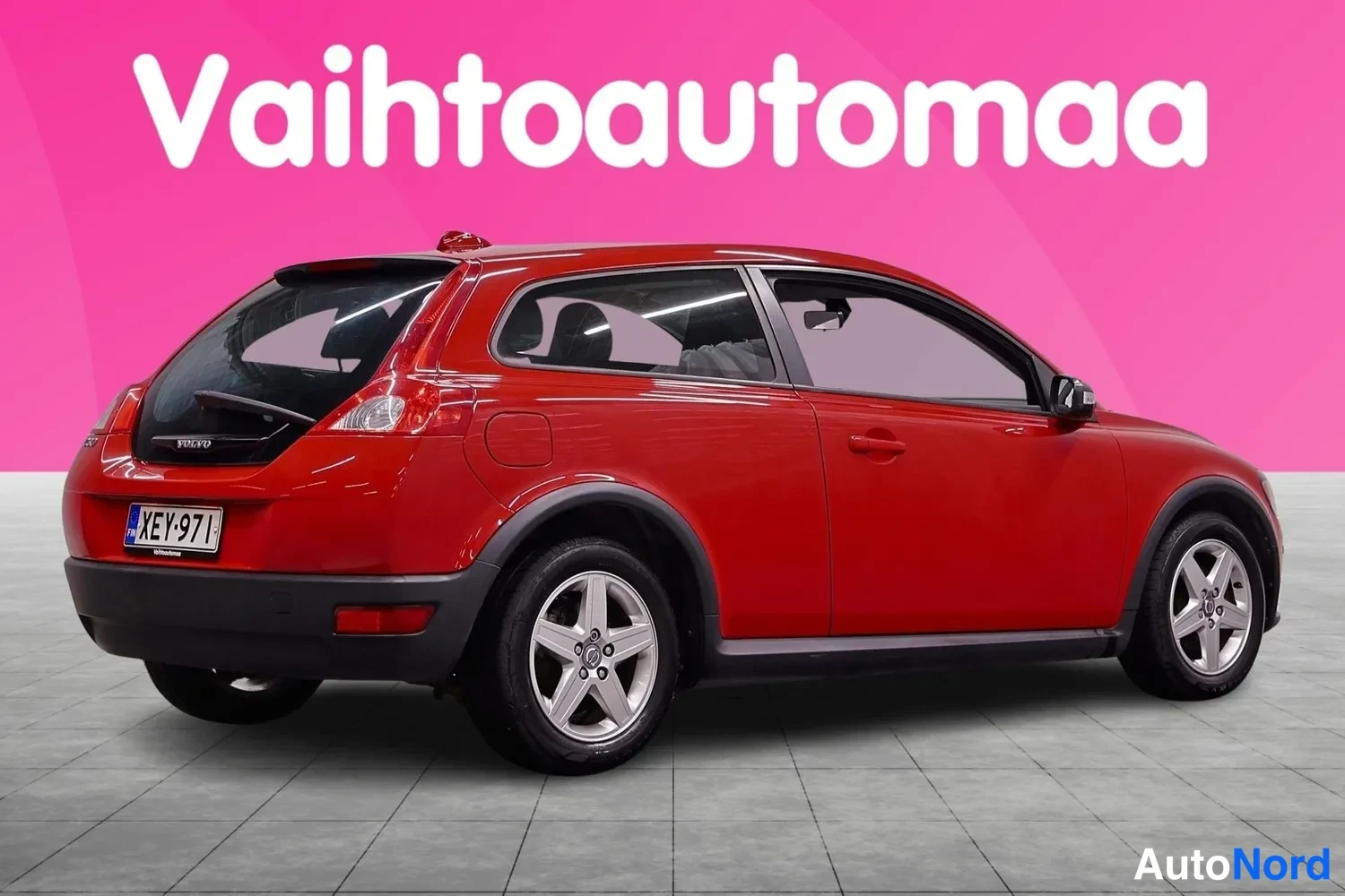 Takaviisto: Punainen kolmiovinen farmarityylinen henkilöauto takaa oikealta kuvattuna, takavalot ja rekisterikilpi näkyvät.