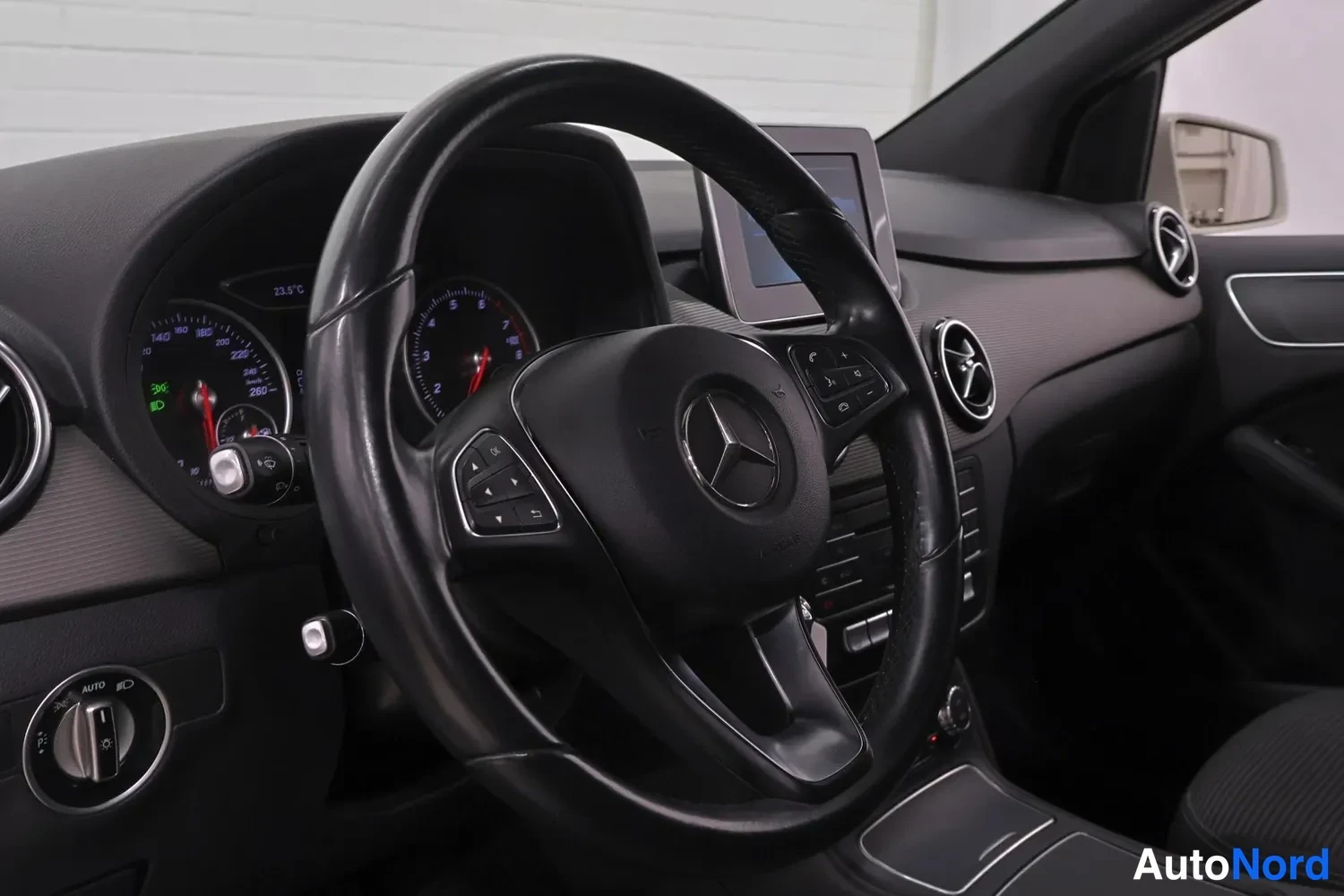 Muu: Mercedes-Benzin ohjauspyörä ja kojelauta: näkyvät Mercedes-tähti, mittarit ja keskellä näyttö sekä ilmastointisäätimet.