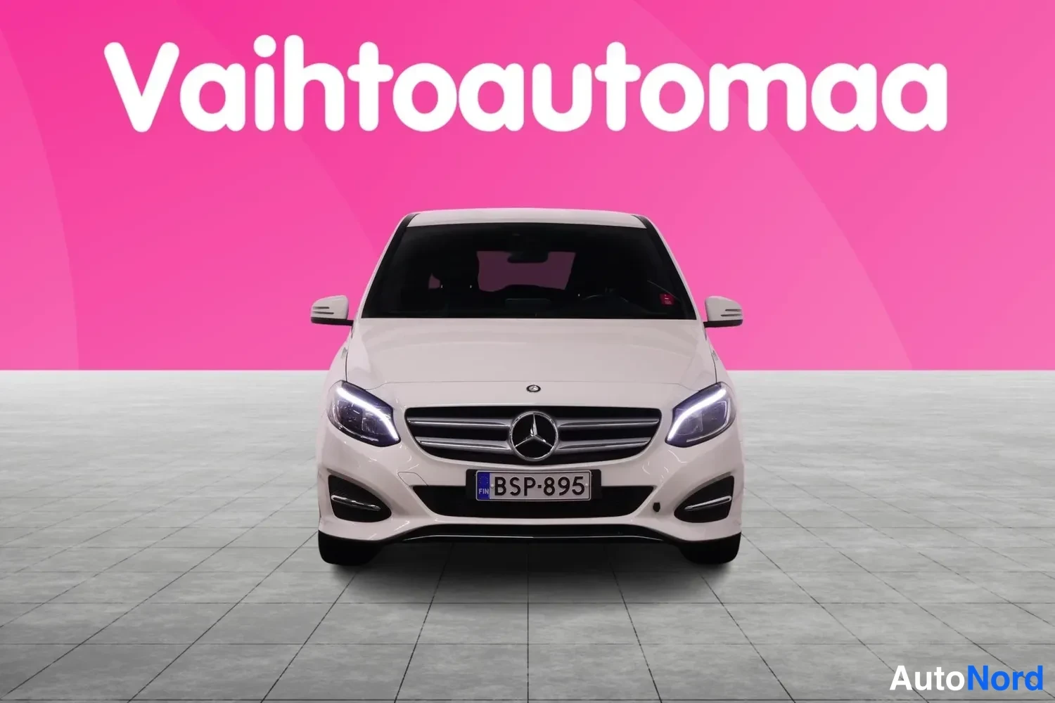 Edestä: Valkoisen Mercedes-Benz B-sarjan auton suora etunäkymä, etusäleikkö ja merkki näkyvät keskellä.