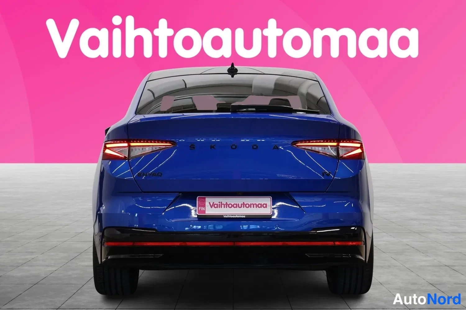 Takaa: Sininen auto kuvattuna suoraan takaa: kapeat takavalot, takaluukussa SKODA-teksti ja Vahtoautomaa-kyltti rekisterin paikalla.
