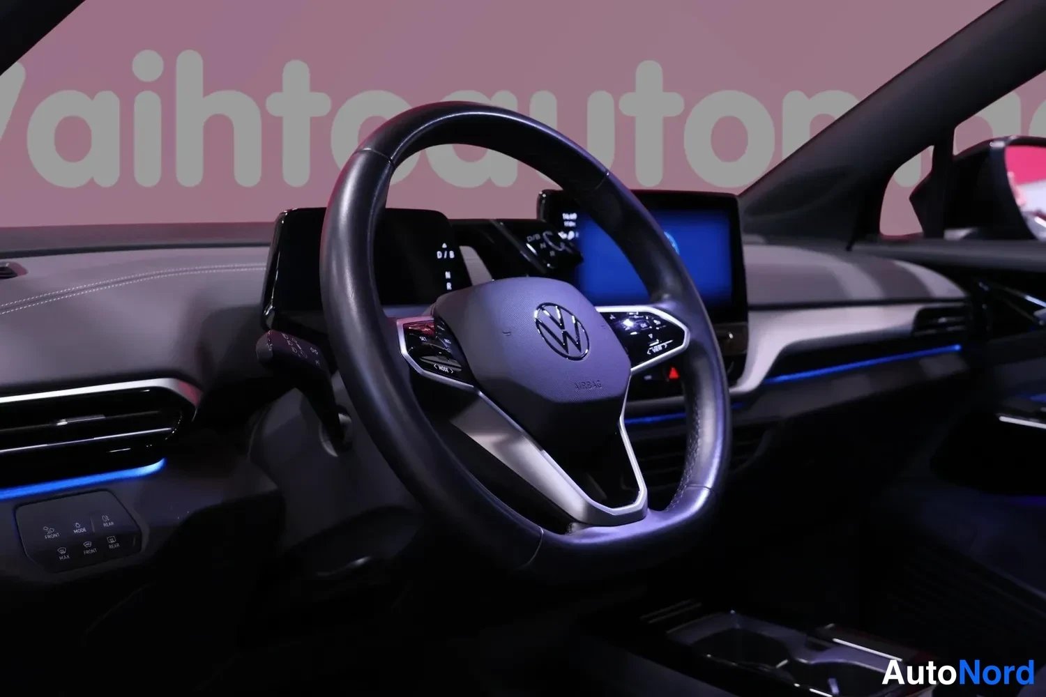 Muu: Volkswagenin ohjaamosta: musta multifunktio-ohjauspyörä ja kosketusnäyttö, sininen tunnelivalaistus kojelaudassa.