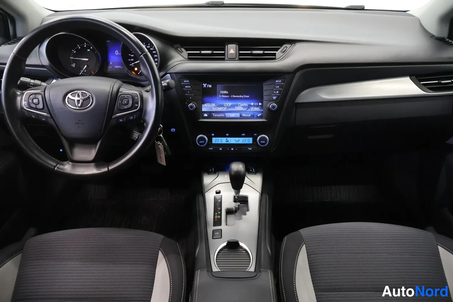 Edestä: Ohjaamo vasemmalta: Toyota-merkkiohjauspyörä, mittaristo, keskikonsolin infotainment-näyttö ja automaattivaihteiston valitsin, edessä kaksi kangasistuinta.