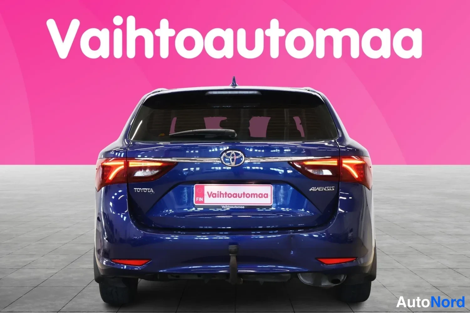 Takaa: Sininen Toyota Avensis -farmari suoraan takaa katsottuna, takaluukussa Toyota-merkki ja AVENSIS-teksti.