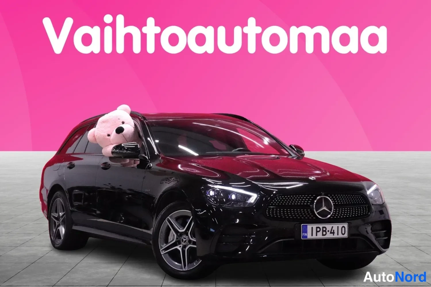 Etuviisto, nokka oikealle: Musta Mercedes-Benz farmari vinosti etuvasemmalta kuvattuna, pinkki tausta.