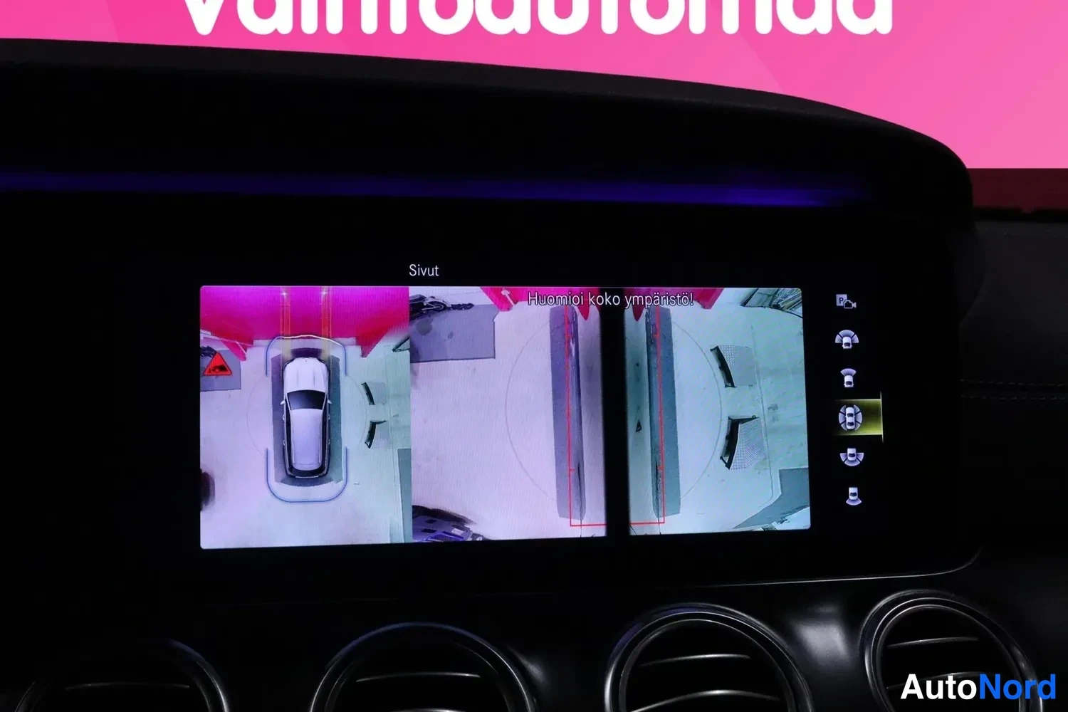 Muu: Infotainment-näyttö näyttää sivukameroiden kuvan ja teksti 'Huomioi koko ympäristö!'.