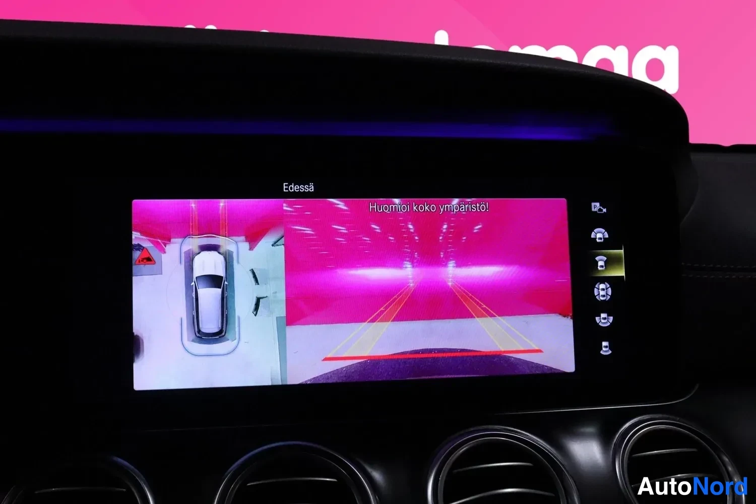 Muu: Infotainment-näyttö näyttää etukameran kuvan ja teksti 'Edessä', 'Huomioi koko ympäristö!'.