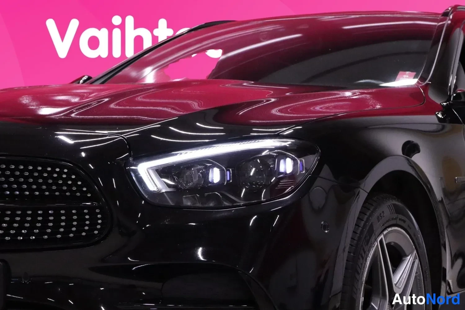 Edestä: Lähikuva mustan Mercedes-Benzin etupäästä ja etupyörästä, etummaisen valon LED-päiväajovalo sytytetty.