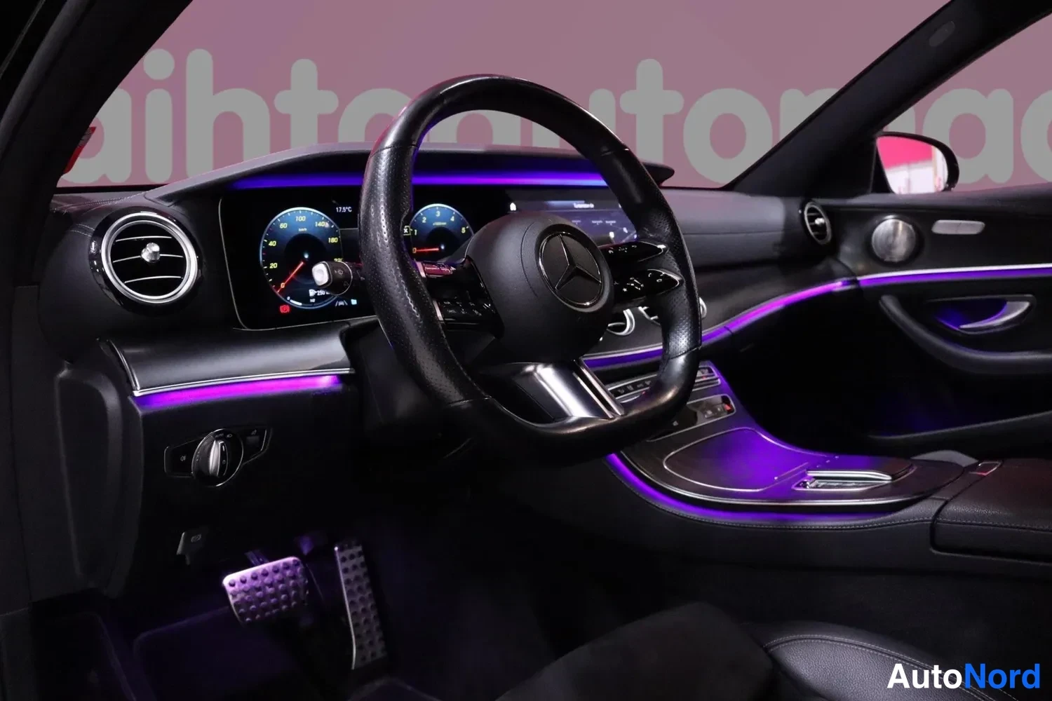 Yksityiskohta: Mercedes-ohjauspyörä, digitaalinen mittaristo ja vihreä-valkoinen näyttö, violetti sisävalaistus.