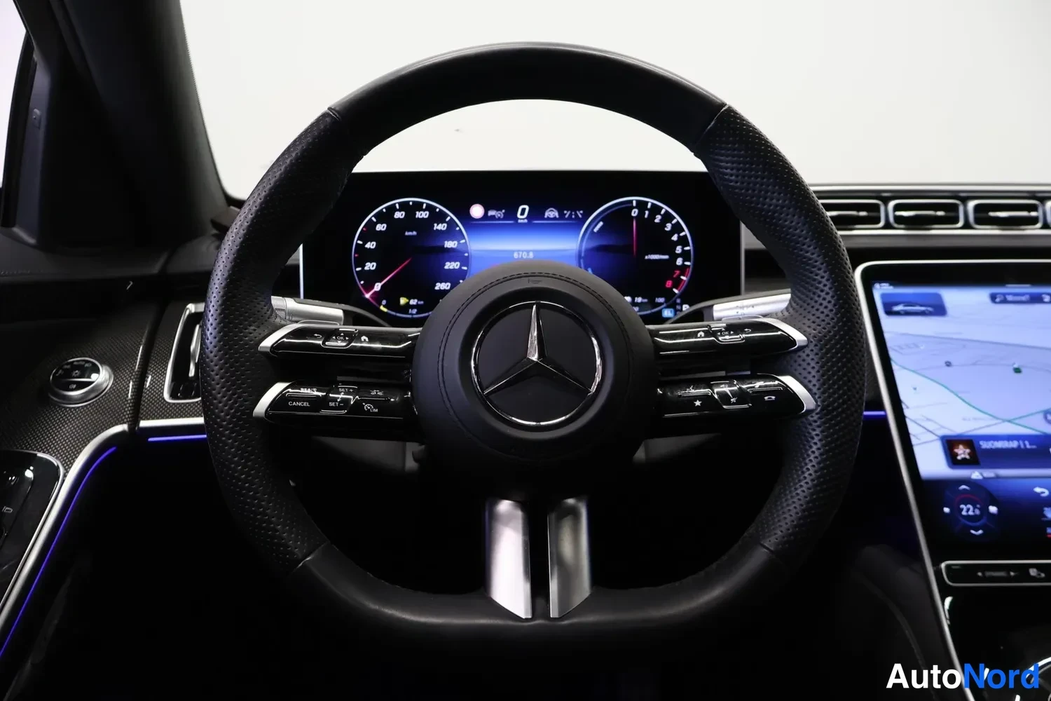 Muu: Ohjaamokuva: Mercedes-tähtimerkillä varustettu ohjauspyörä, digitaalinen mittaristo ja oikealla kartta näyttävä keskinäyttö.