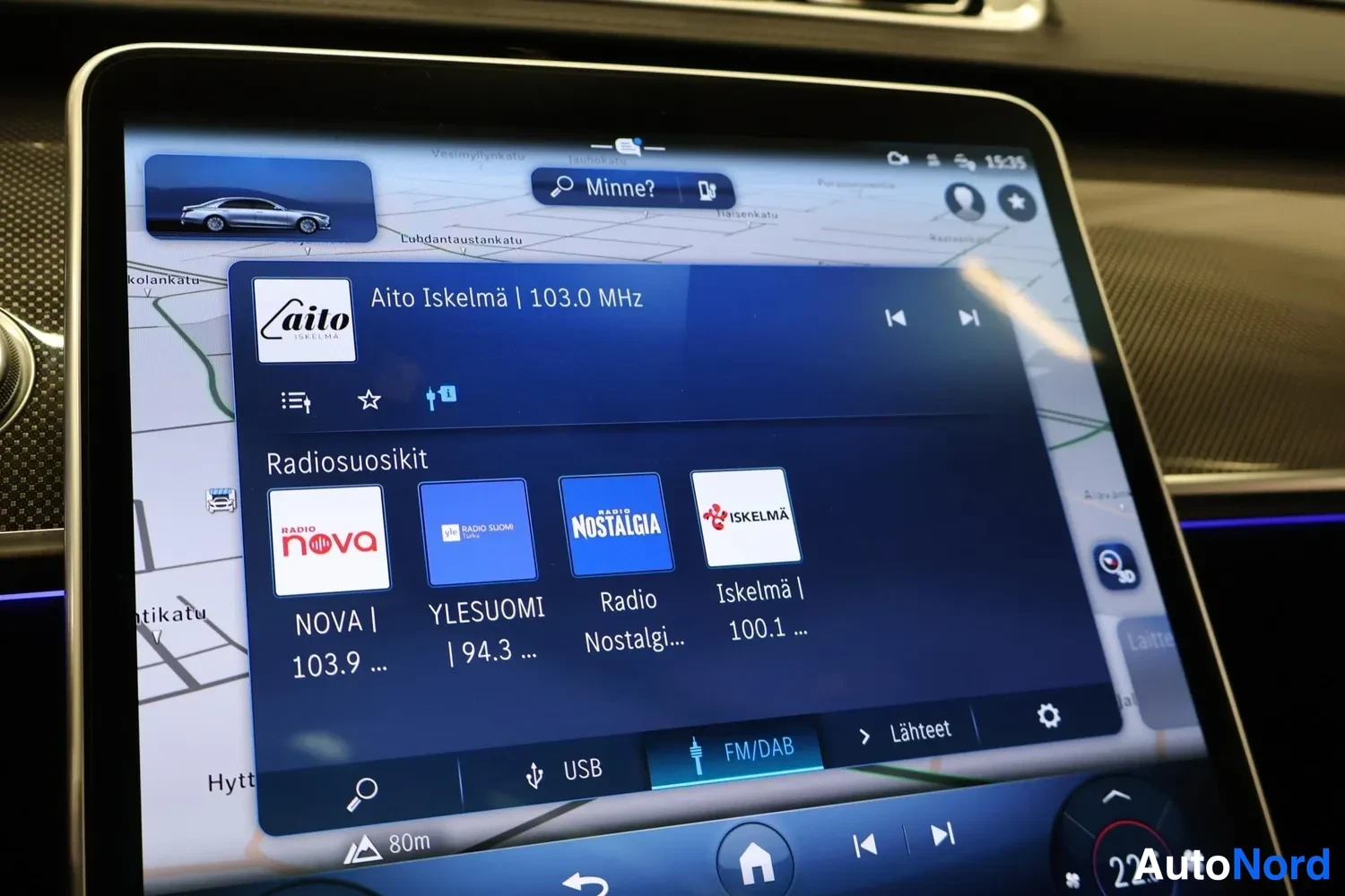 Muu: Infotainment-näytön lähikuva: navigointikartta ja radiovalikko, toistettavana Aito Iskelmä | 103.0 MHz, Radiosuosikit-kohdissa Radio NOVA, YLE SUOMI, Radio Nost