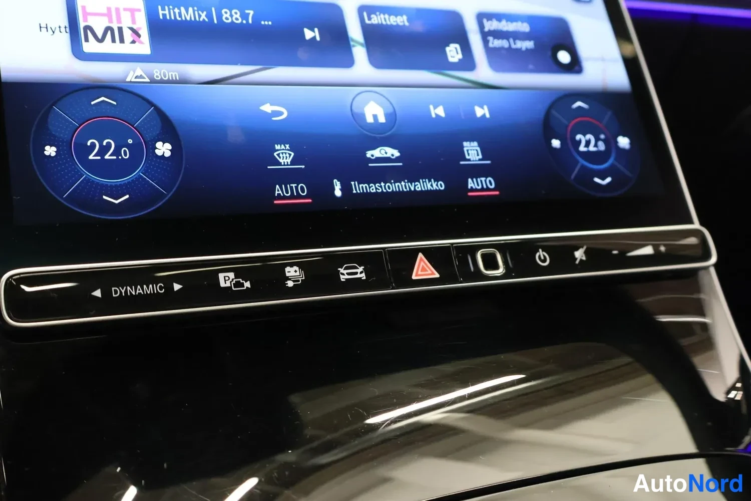 Yksityiskohta: Kojelaudan infotainment-näyttö jaalla, jossa näkyy mediatoisto (HitMix 88.7), kaksivyöhykkeinen ilmastointi 22,0 astetta, Ilmastointivalikko AUTO -asetuksilla j
