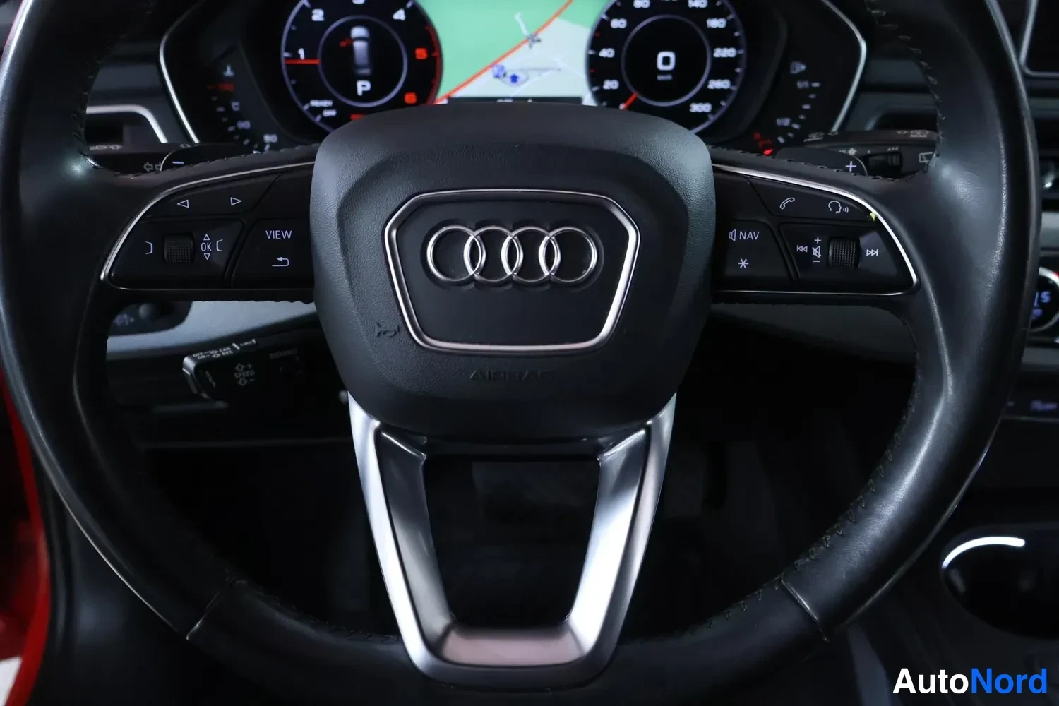 Muu: Ohjauspyörän ja mittariston lähikuva: Audi-merkki, kauko-ohjattu cruise- ja NAV-napit, digitaalinen mittaristo navigointikartalla.