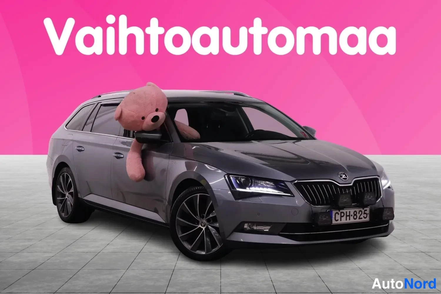 Etuviisto, nokka oikealle: Harmaa farmariauto etukulmasta oikealta, rekisteritunnus, tekonalle takaluukissa vaaleanpunaisella taustalla.