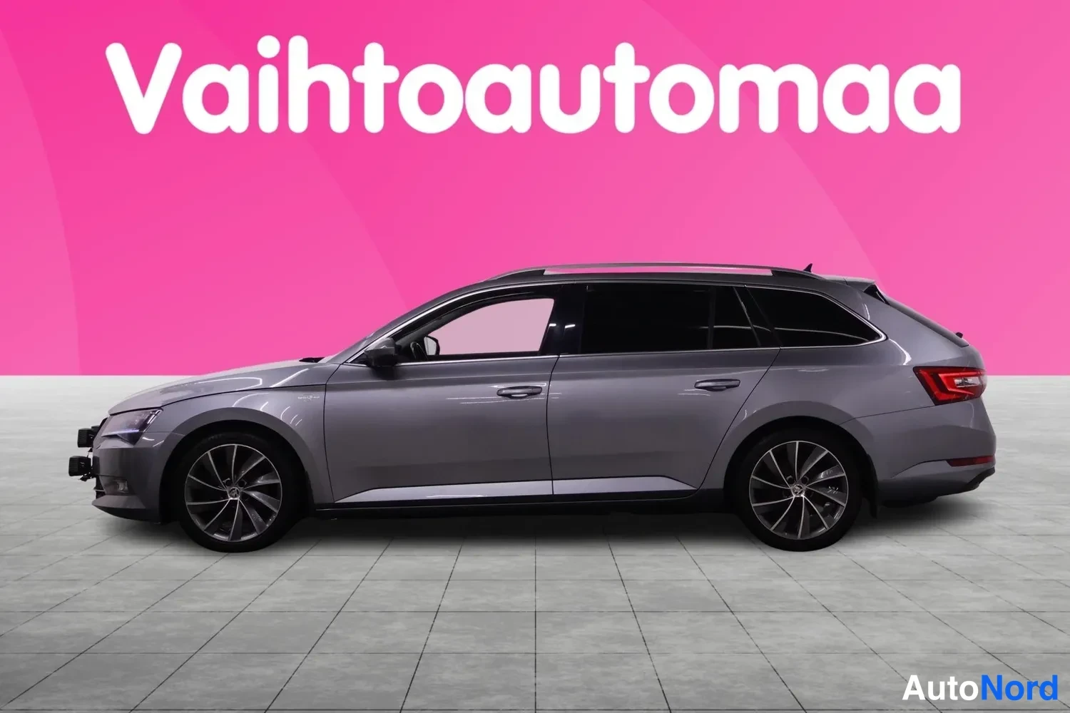 Sivulta: Auton sivukuva: harmaan farmariautoa vasemmalta taaksepäin, pinkki tausta ja kirjoitus Vaihtoautomaa.