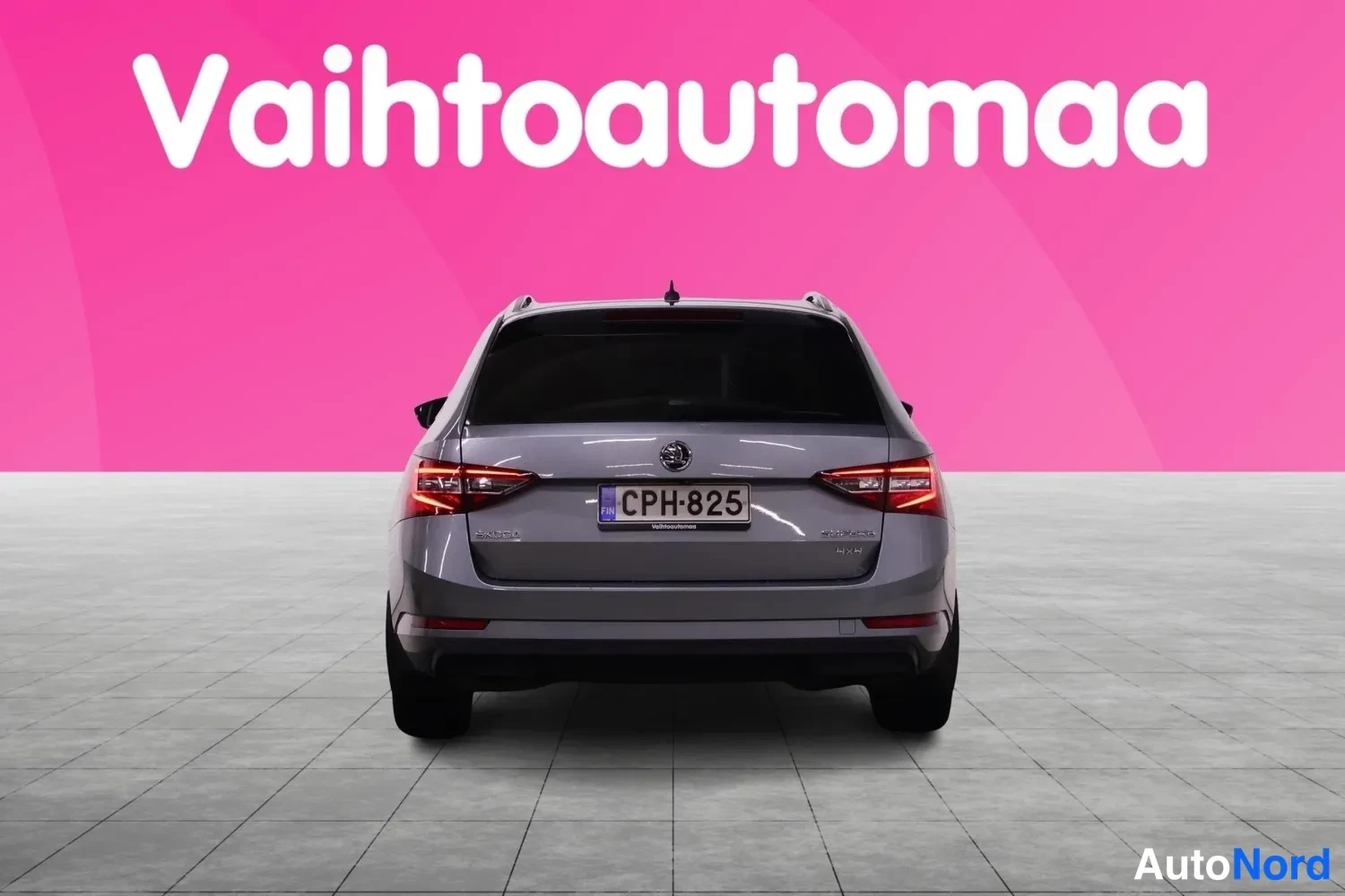 Takaa: Auton takakuva suoraan takaa: harmaan farmariauto takanäyttö, takavalot ja rekisteri.