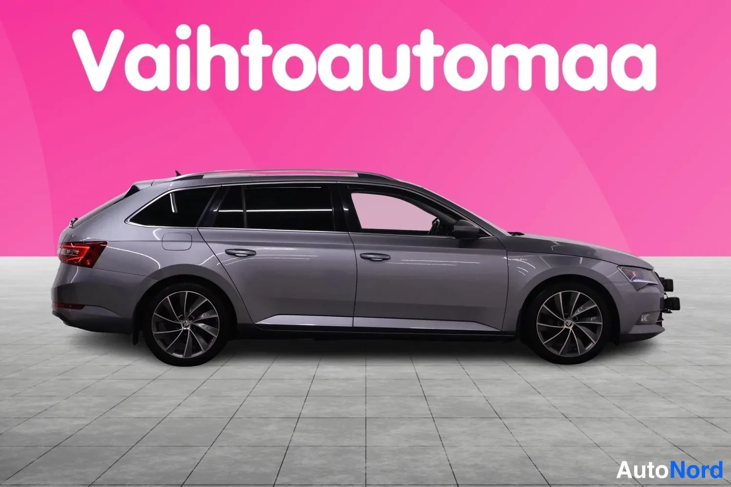 Sivulta: Auton sivukuva: hopeanharmaa farmarikorinen auto leveässä sivuprofiilissa, kevytmetallivanteet ja kattokaiteet näkyvät.
