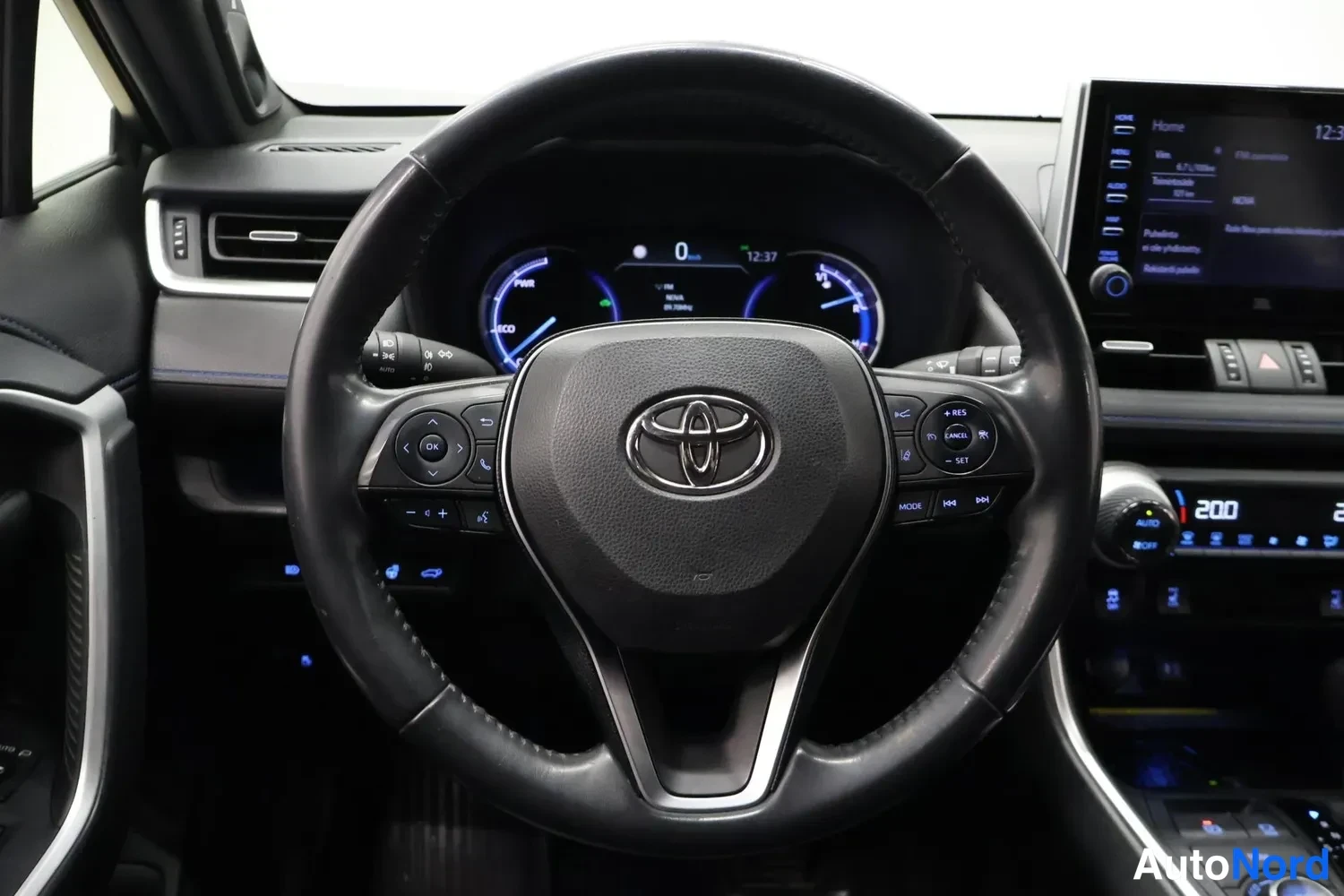Yksityiskohta: kuljettajan paikan ohjauspyörä Toyota-merkillä, osittain hybridin mittaristo ja keskikonsolin kosketusnäyttö näkyvät.