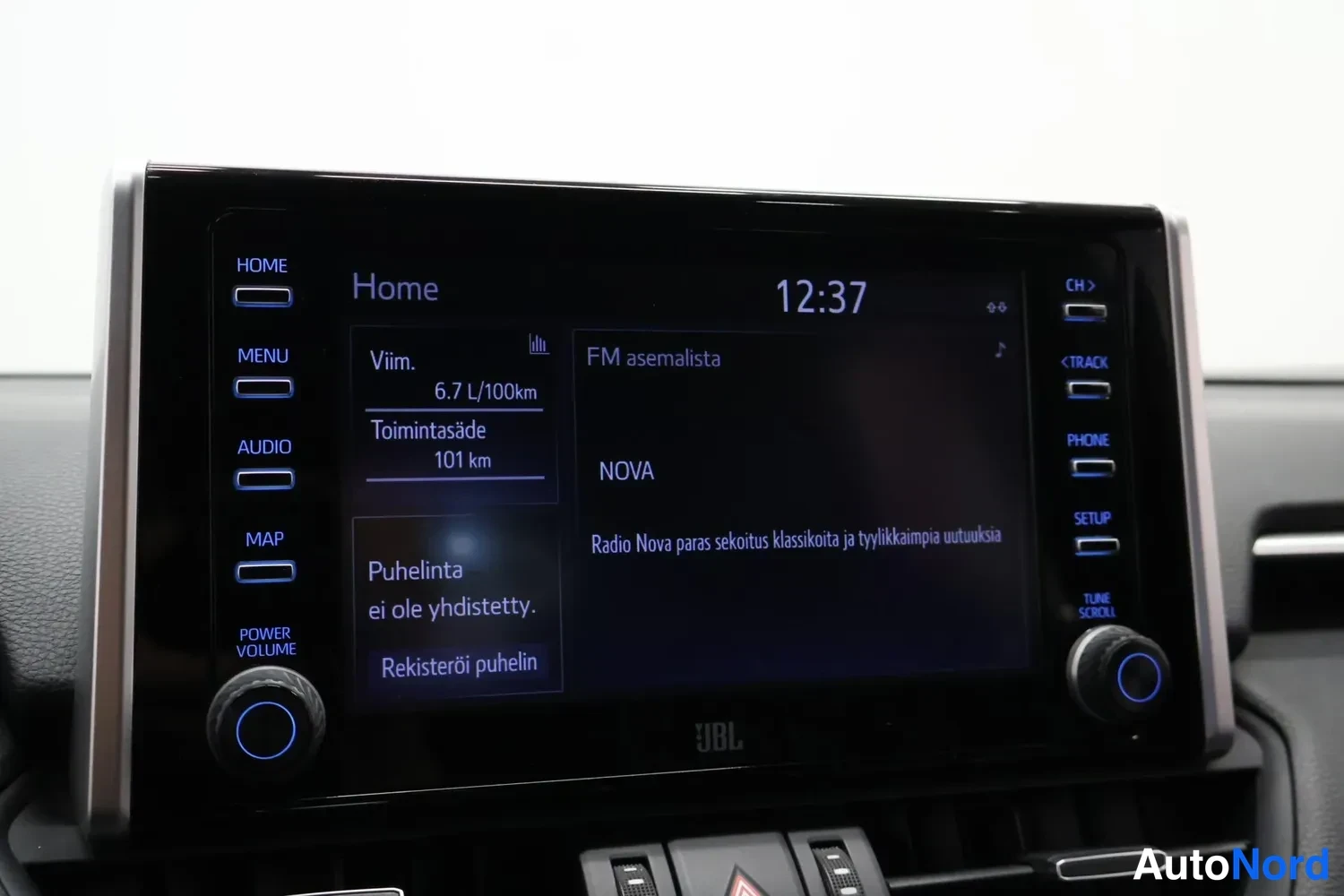 Yksityiskohta: Auton kojelaudan kosketusnäyttö Home-näkymässä: kello 12:37, viime kilometrien keski kulutus 6,7 l/100 km, toimintasäde 101 km, FM-asemalista ja radioasema NOVA