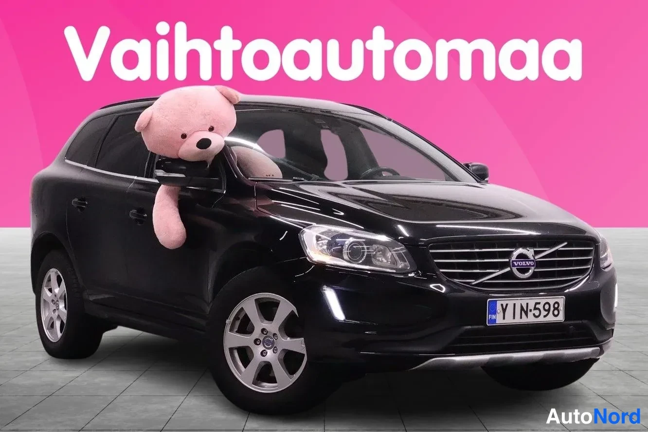 Etuviisto, nokka oikealle: Musta Volvo XC60 etukulmasta oikealta, rekisteritunnus, ikkunasta pilkistaa pehmolelu.