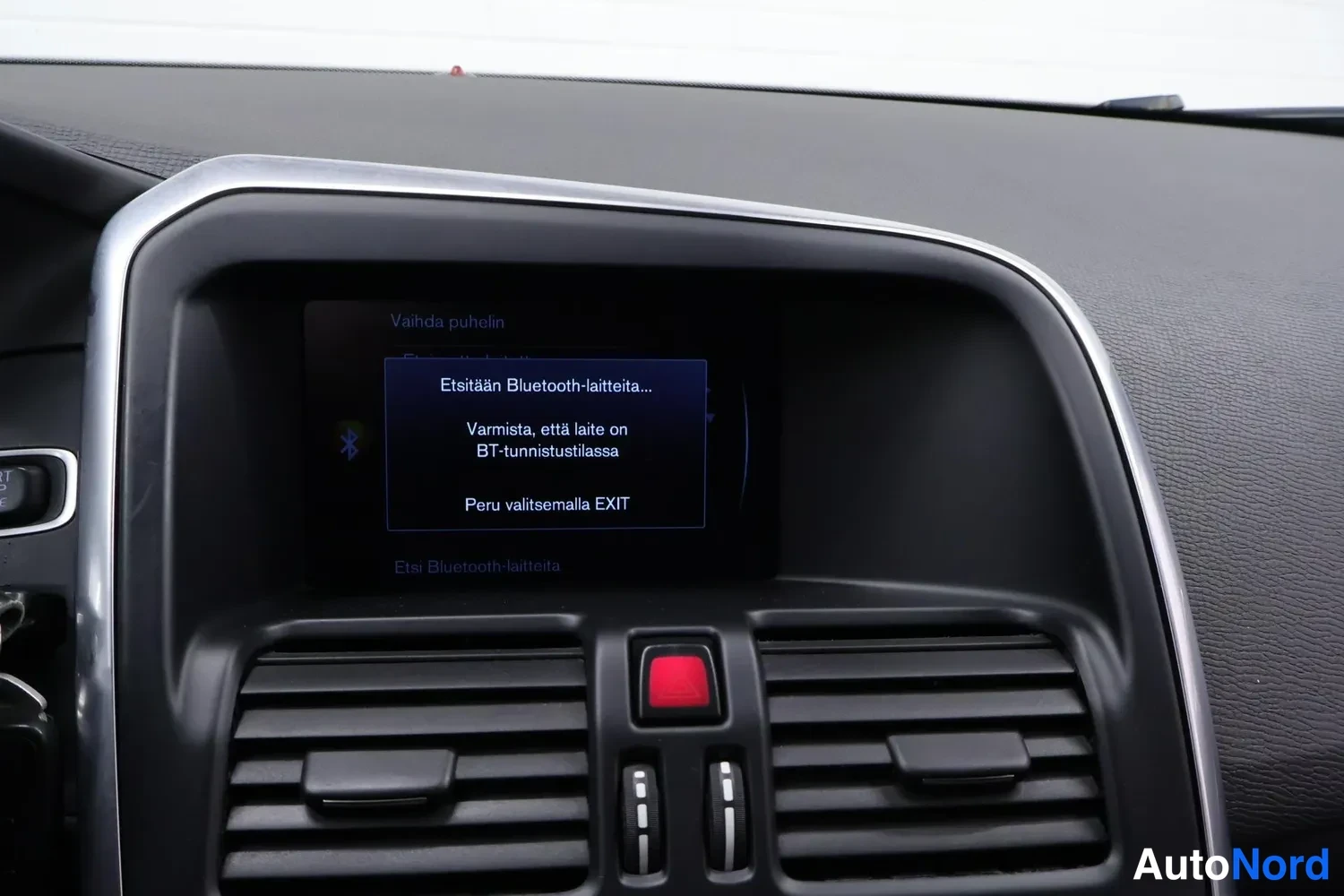 Yksityiskohta: Kojetason näytössä Bluetooth-laitteiden hakuviesti suomeksi; näytön alla ilmastointiautot ja punainen varoitusnappi.
