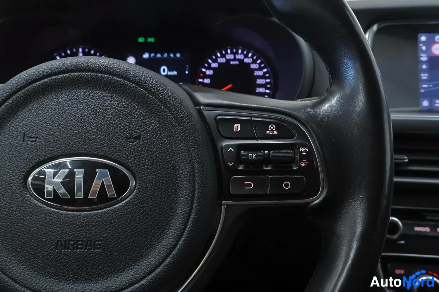 Edestä: Ratin keskellä KIA-logo ja AIRBAG-teksti; ohjauspainikkeet MODE, OK, RES, SET, näytössä 0 km/h ja nopeusmittari.