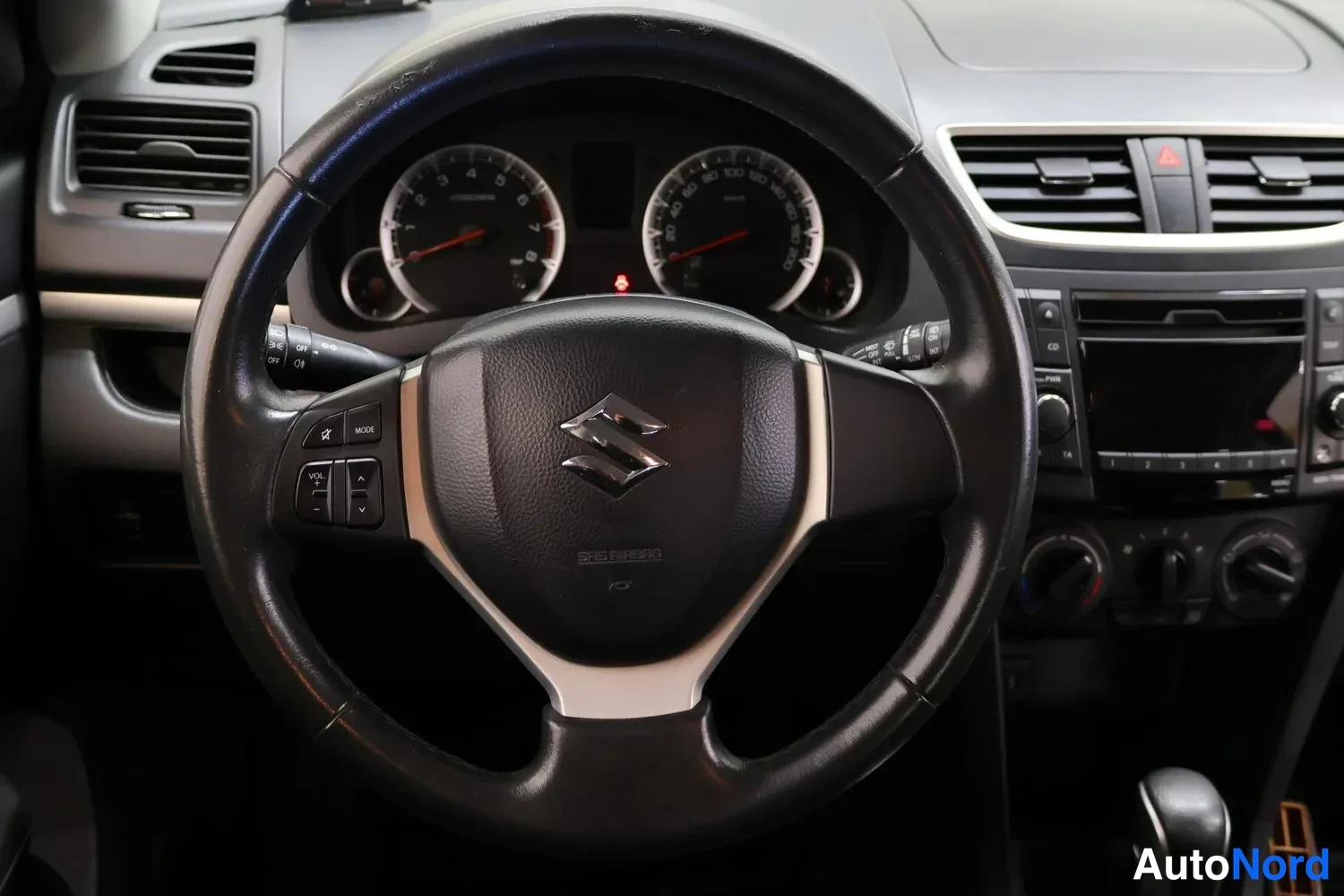 Yksityiskohta: Suzukin ohjaamo: ratissa audio- ja puhelinpainikkeet, mittaristo ja automaatgivaihtajan vipu näkyvät.
