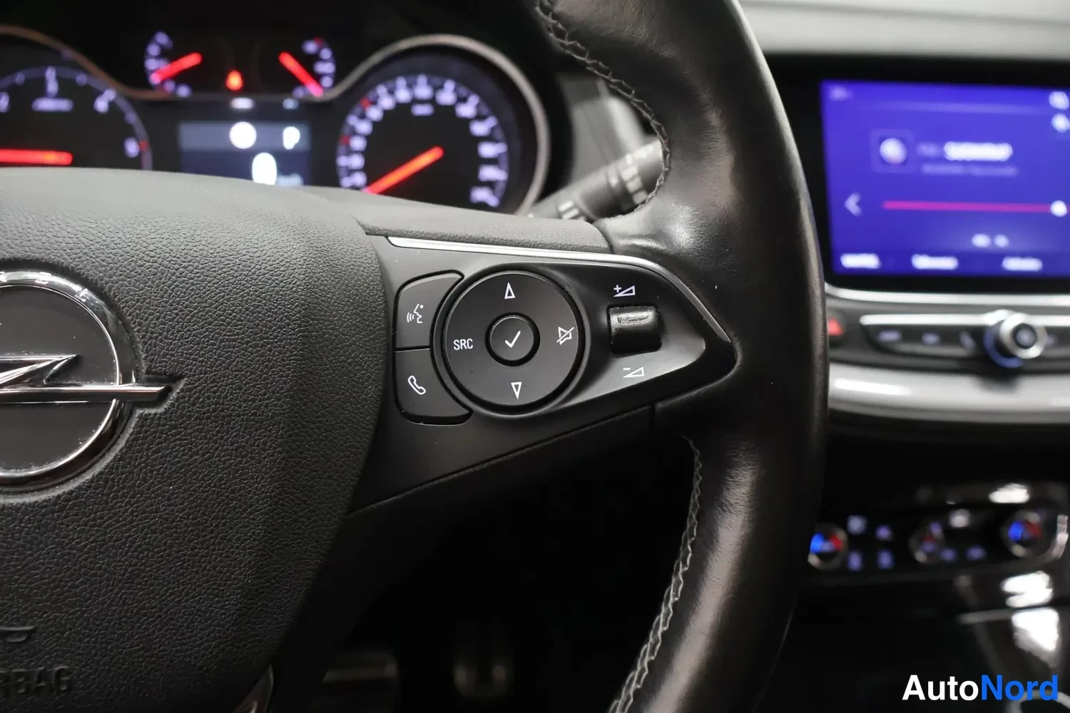 Muu: Rattipöydän oikeanpuoleiset hallintapainikkeet, Opel-tunnuksella varustettu ohjauspyörä ja kojelaudan näytöt lähikuvassa.