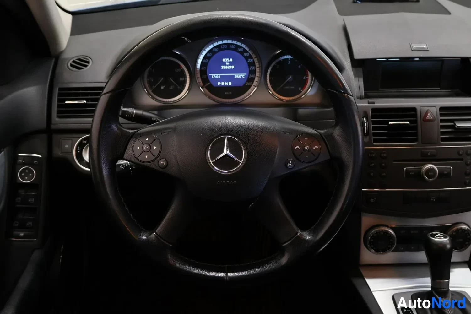 Muu: Ohjaamo Mercedes-Benzissä: ohjauspyörä ja kojelauta, mittariston näytössä lukemat 832,8 km ja 3302/19, kellonaika 17:01 ja lämpötila 24,0 °C.