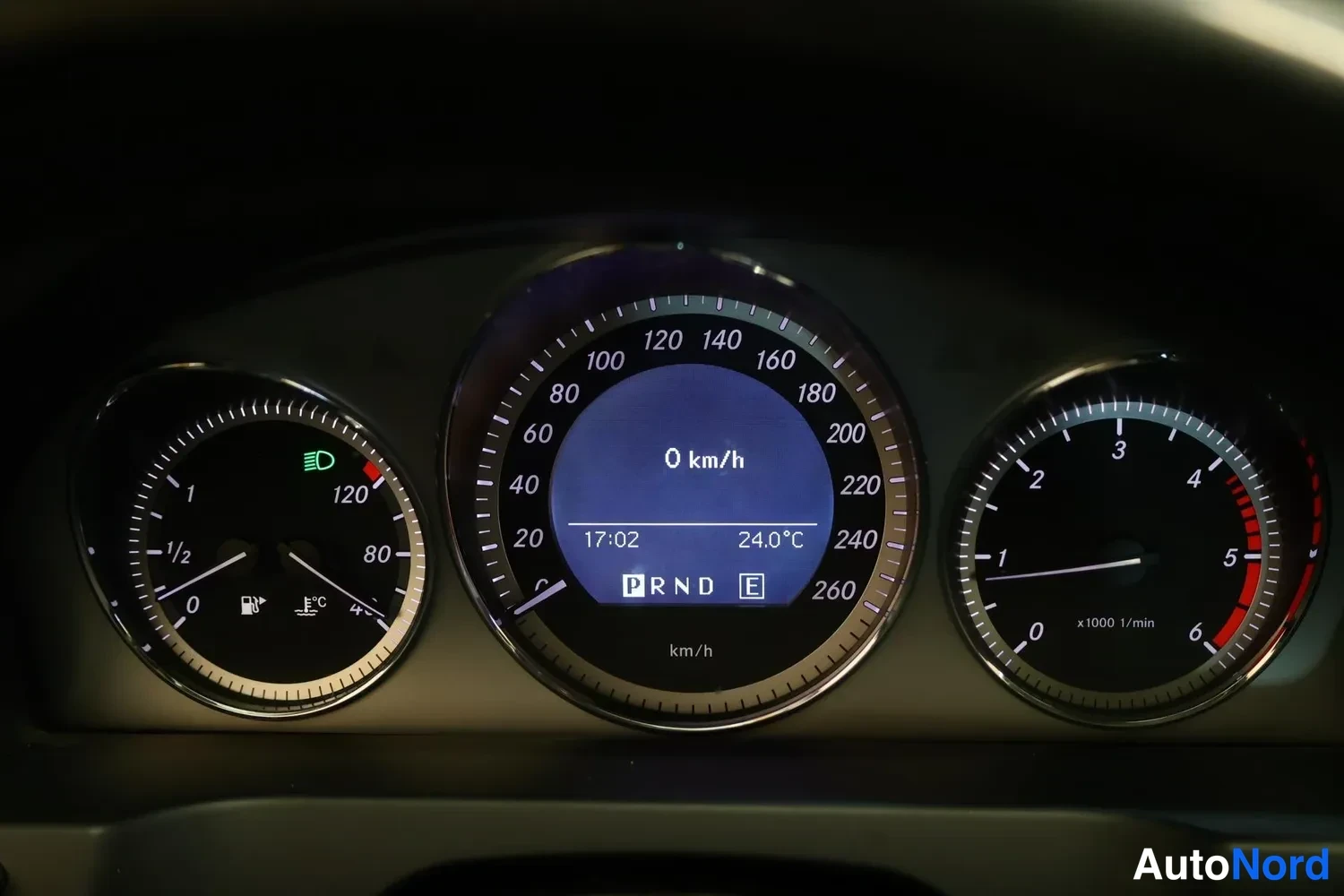Muu: Mercedes-Benzin mittaristo lähikuvassa: nopeusmittari näyttää 0 km/h, kellonaika 17:02, lämpötila 24,0 °C ja vaihteisto P. Polttoaineneedelmä noin puolivälissä.