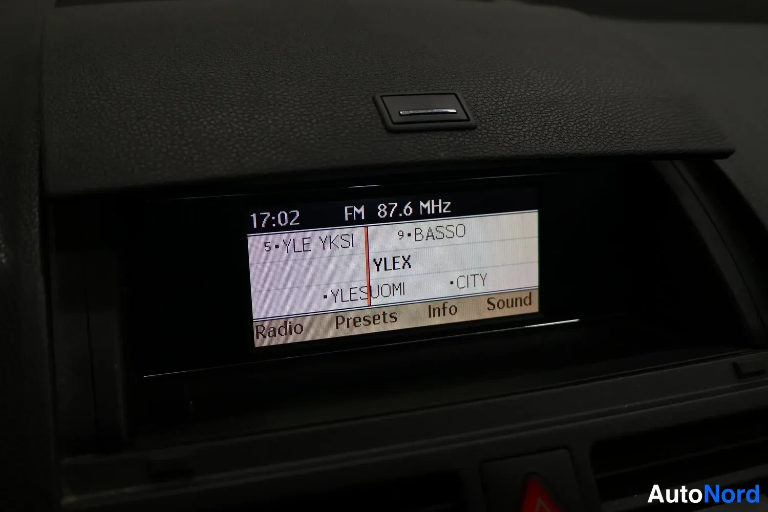 Muu: Mercedes-Benzin radiolaitteen näyttö: kello 17:02, FM 87,6 MHz ja kanavalistaus.