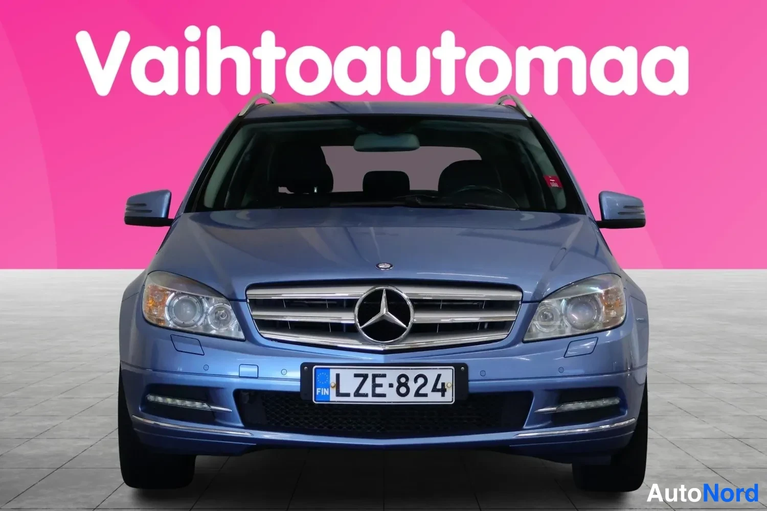Edestä: Sinisen Mercedes-Benzin etupää suoraan edestä, tunnus, vaaleanpunainen tausta.