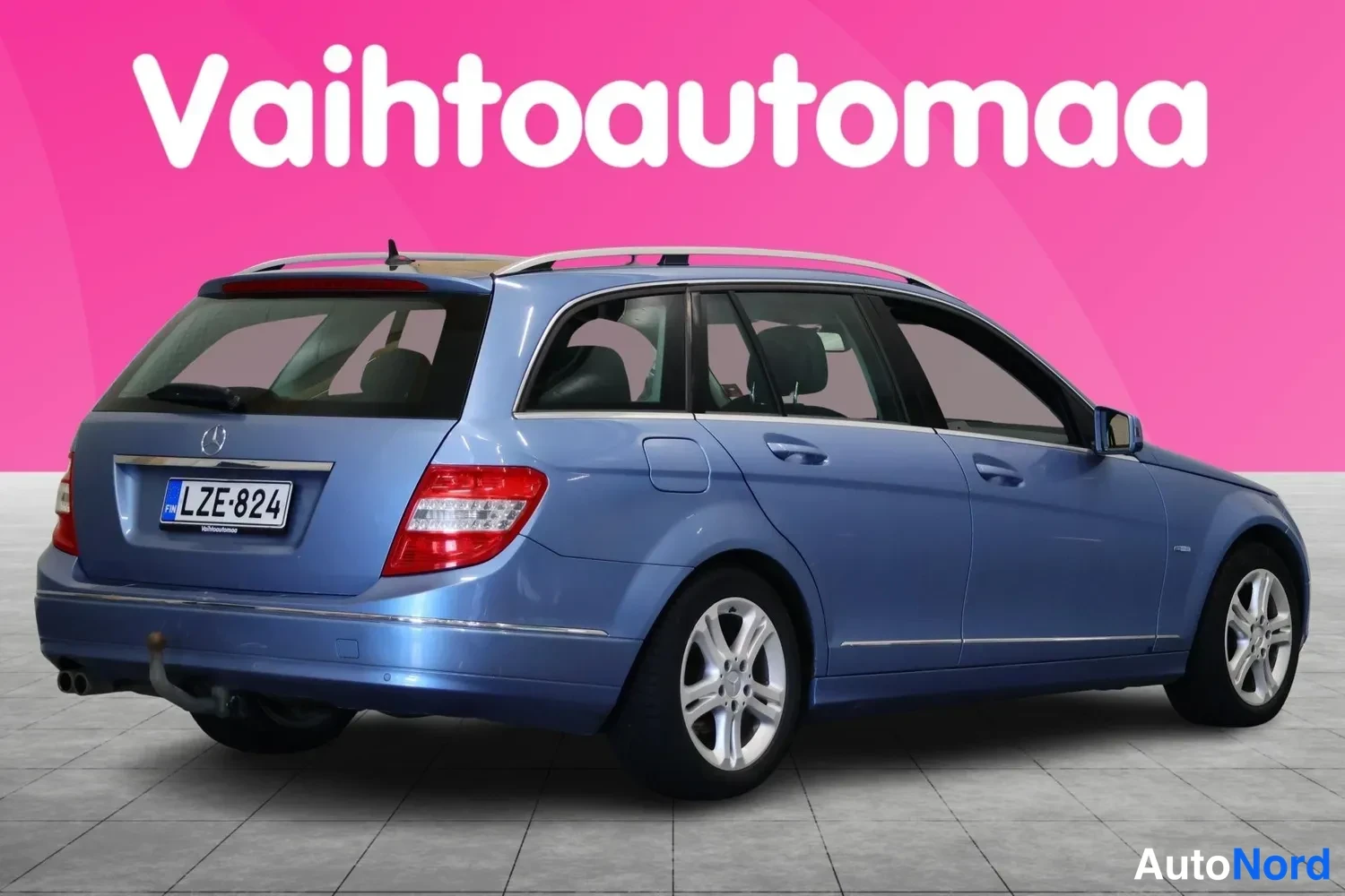 Takaviisto: Sininen Mercedes-Benz C -asema-auto takaa viistosti kuvattuna, rekisteritunnus, takavalo ja luvat kytketty.