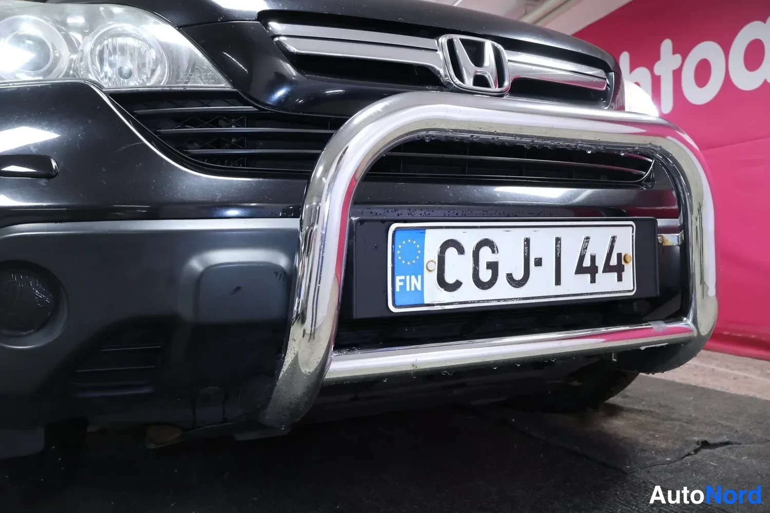 Edestä: Auton etupään lähikuva: Honda-merkki etusäleikössä, krominen etukaariputki puskurin edessä ja rekisterikilpi.