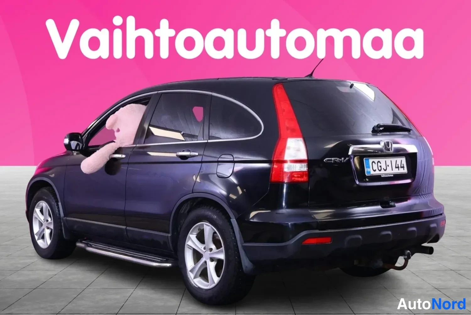 Takaviisto: Musta Honda CR-V takaviistosta oikealta, valoisa pinkki tausta.