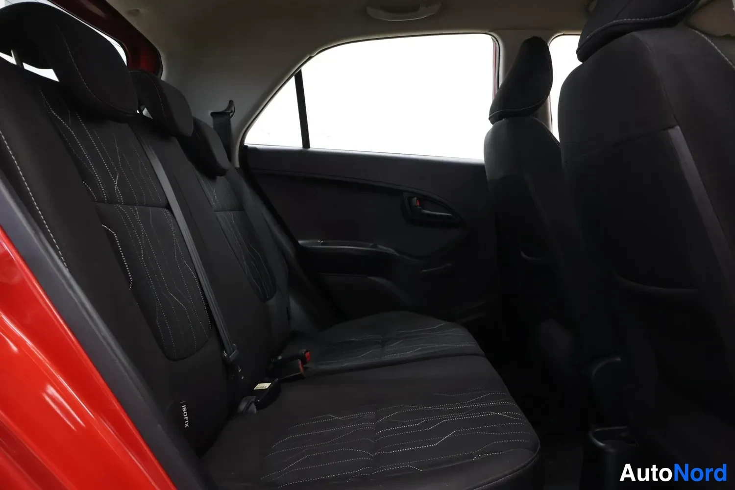 Muu: Takaistuimen sisäkuva mustasta kankaasta valkoisin ompelein; takaoven paneli, turvavyöt ja ISOFIX-merkintä näkyvät.