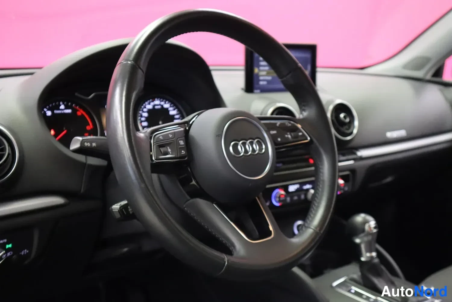 Muu: Audi-ohjauspyörä ja kojelauta lähikuvassa, mittarit ja keskikäyttöpaneeli näkyvissä.